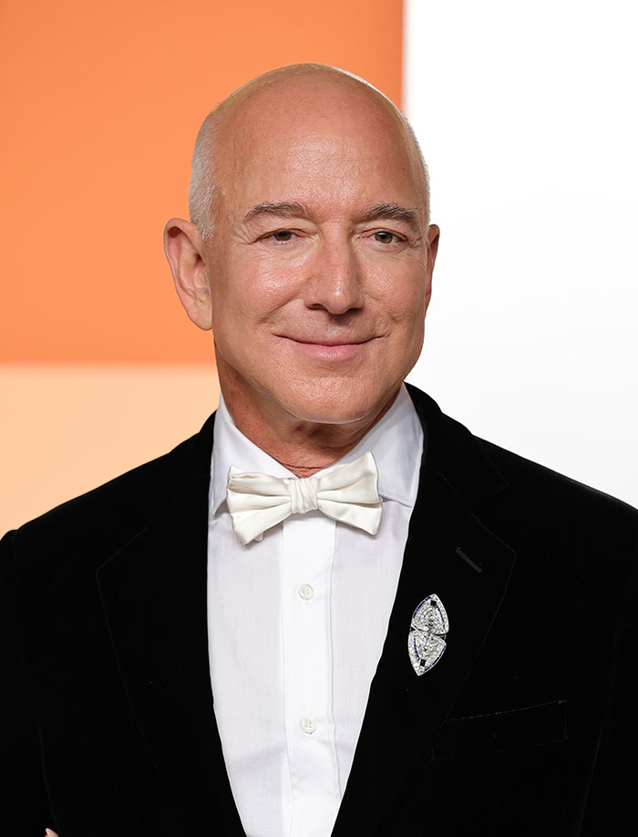 Jeff Bezos in a black tuxedo and white bow tie, smiling against an orange and white background, related to Sydney Sweeney business. Jeff Bezos in a black tuxedo and white bow tie, smiling against an orange and white background, related to Sydney Sweeney business.