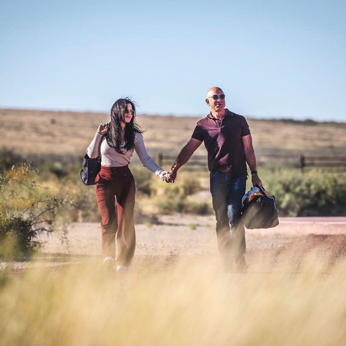 Jeff Bezos walking hand in hand with Lauren S&aacute;nchez in a desert setting, showing his changed hair look.