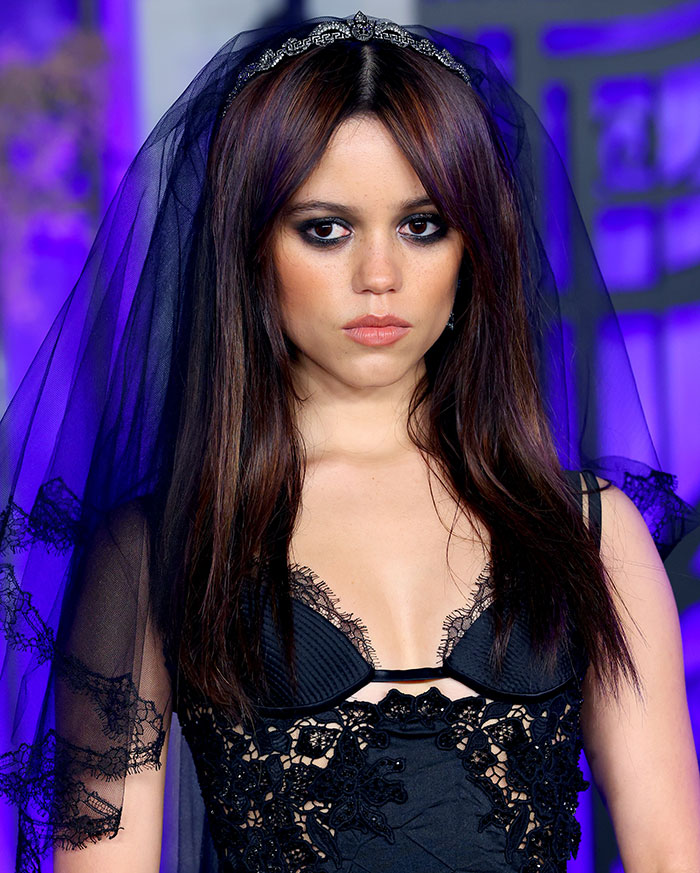 Jenna Ortega wearing a black sheer dress with lace details and a veil at the Wednesday premiere, showcasing the sheer dress trend. Jenna Ortega wearing a black sheer dress with lace details and a veil at the Wednesday premiere, showcasing the sheer dress trend.