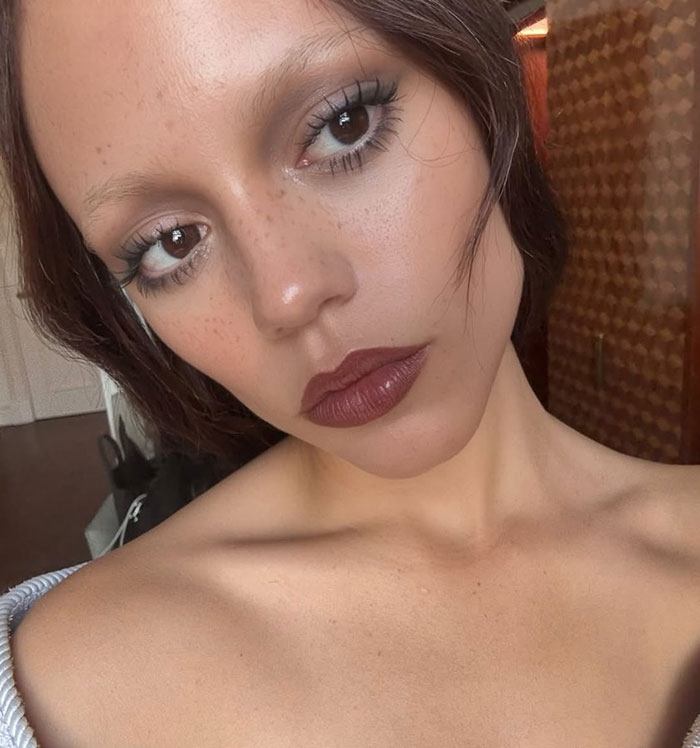 Close-up of Jenna Ortega showcasing a sheer dress trend with natural makeup and soft lighting indoors. Close-up of Jenna Ortega showcasing a sheer dress trend with natural makeup and soft lighting indoors.