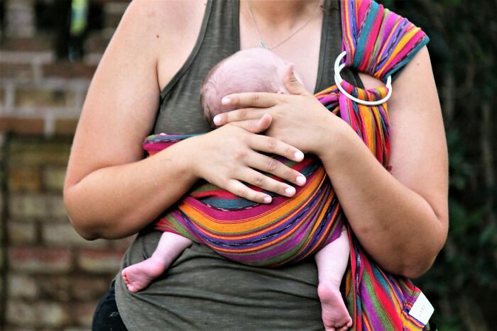 Mother carrying newborn baby in a colorful wrap, illustrating common challenges and comments women face after birth.