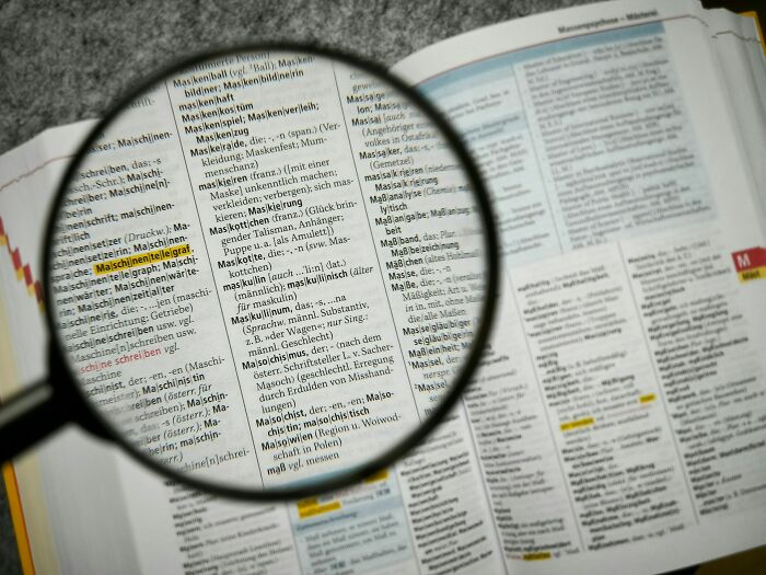 Magnifying glass focusing on text in a dictionary, illustrating careful and calm communication skills concept.