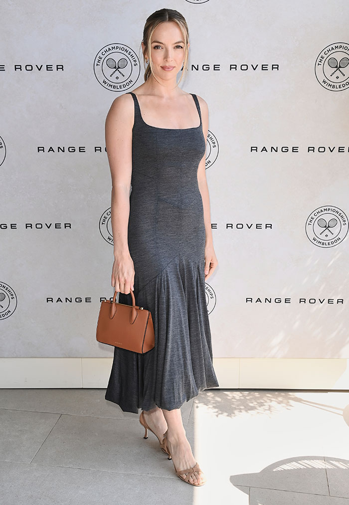 Woman in a gray dress and heels holding a brown handbag at a Wimbledon 2025 event with Range Rover backdrop.