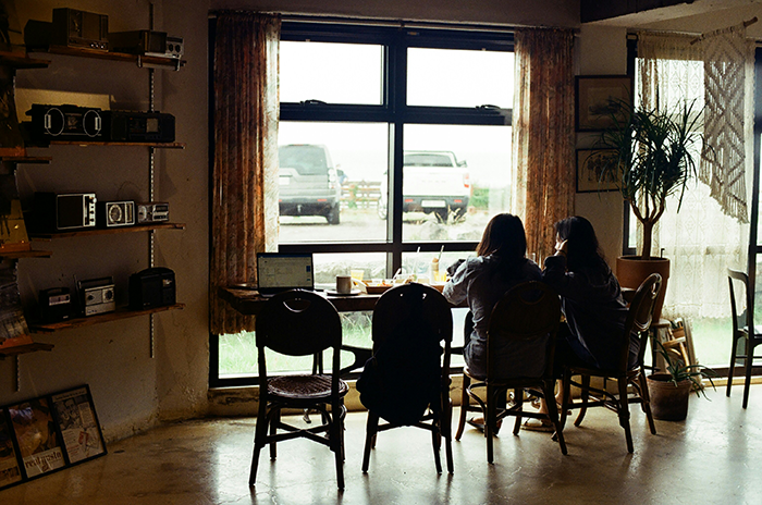 Two women seated indoors by a window, reflecting on a 30-year-old friendship and wedding tension over weight loss. Two women seated indoors by a window, reflecting on a 30-year-old friendship and wedding tension over weight loss.