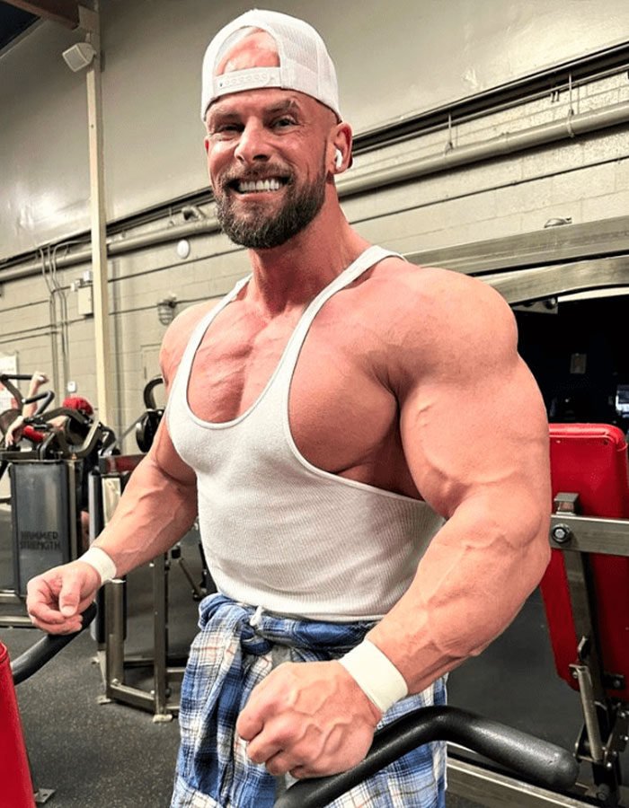 Muscular Joey Swoll in a gym wearing a white tank top and backwards cap, responding after Hulk Hogan memorial backlash.