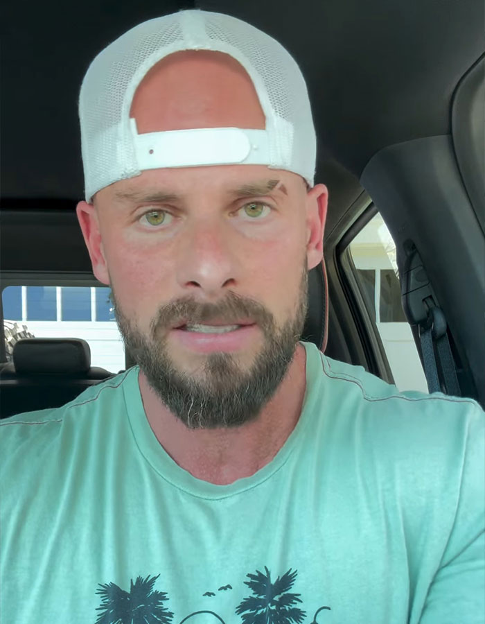 Joey Swoll wearing a white cap backward and a green shirt, filming a groveling apology video inside a vehicle.