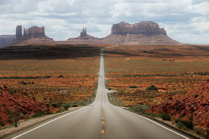 Long open road leading to red rock formations in a desert landscape, capturing travelers' surprising things about the U.S.