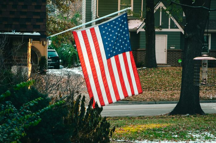American flag hanging outside a suburban house, symbolizing travelers' surprising discoveries about the U.S. when they visit.
