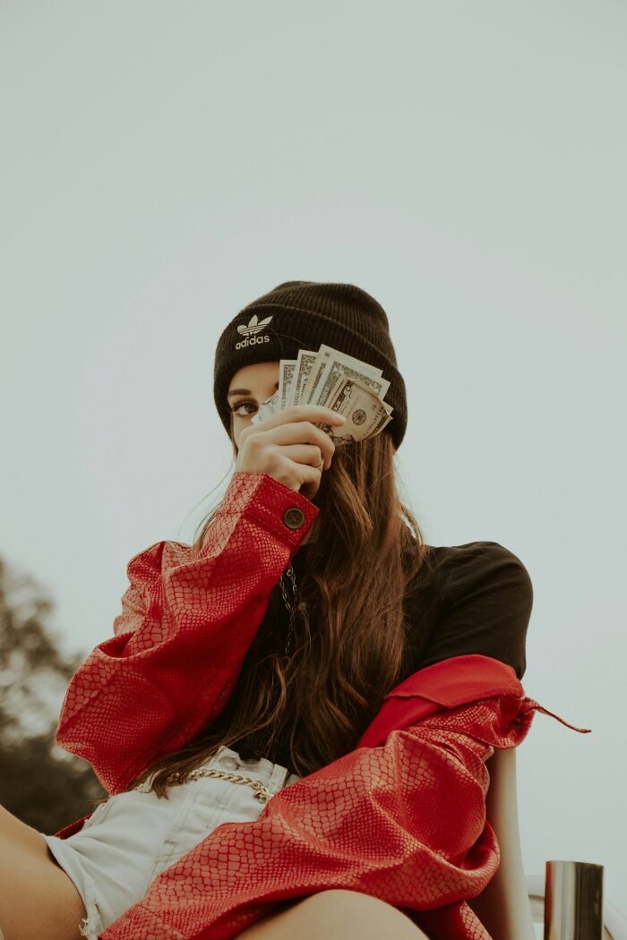 Young woman in a black beanie and red jacket holding cash, illustrating stories about awful roommates and difficult living situations.
