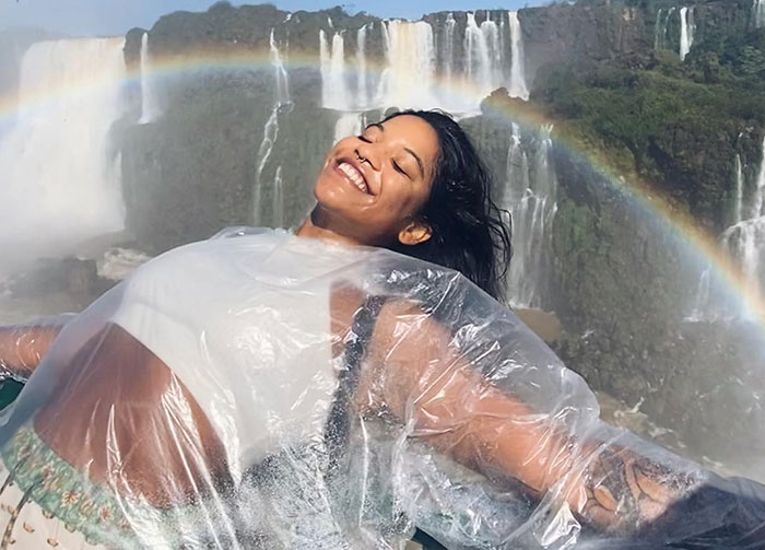 Smiling woman enjoying waterfall view with rainbow, unrelated to autopsy of tourist who fell into volcano SEO keywords.