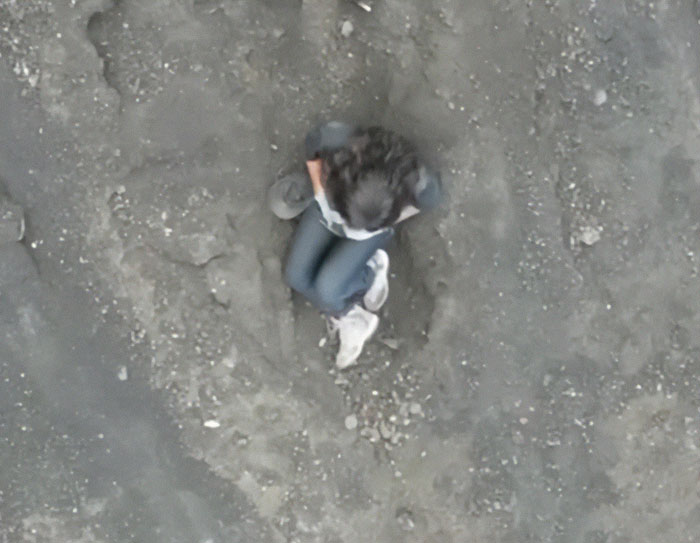 Overhead drone image of a tourist sitting on rocky volcanic terrain moments before falling into volcano.