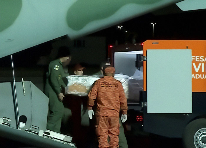 Emergency responders in uniforms carry a covered stretcher at night related to autopsy of tourist who fell into volcano