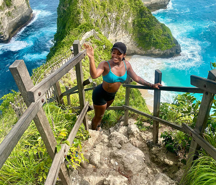 Tourist hiking steep volcanic cliffs near ocean with lush greenery and clear blue waters in the background.