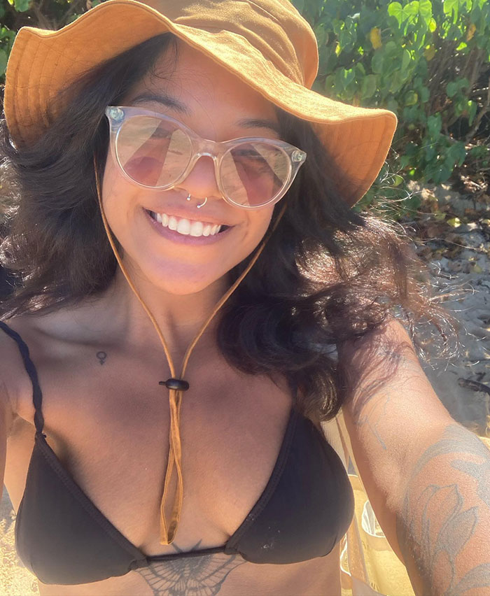 Young female hiker wearing a sun hat and sunglasses smiling outdoors, related to abandoned inside active volcano news.