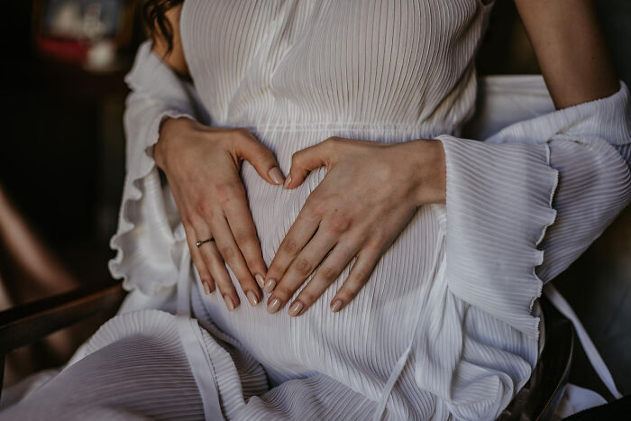 Pregnant woman in white pleated dress making a heart shape on her belly, symbolizing bravery and change in history. - 10