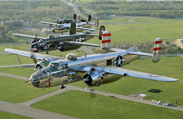 Three vintage WWII bomber planes flying in formation over green fields demonstrating bravery in history. - 19