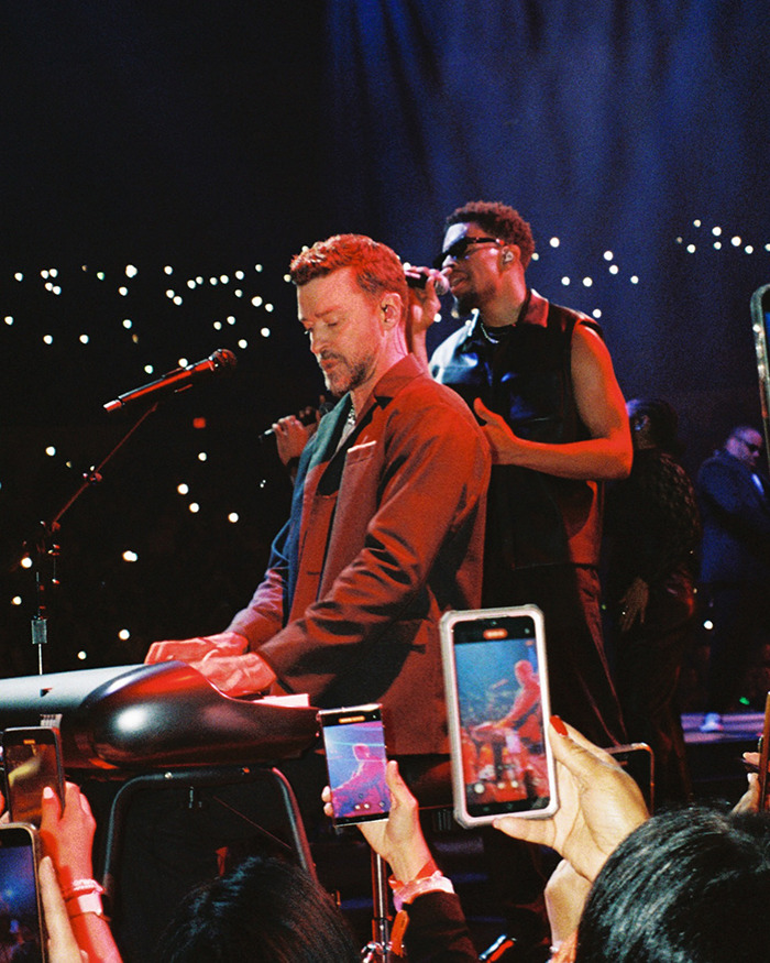 Justin Timberlake performing on stage with band, amid crowd capturing the concert on smartphones. - 3