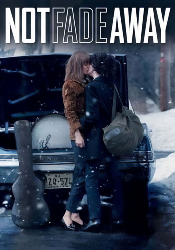 Acotrs sharing a kiss in a snowy street scene with a guitar case and open car trunk nearby, Not Fade Away film.