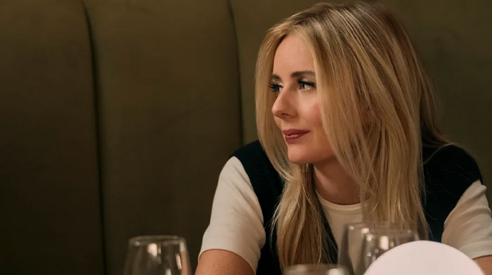 Justine Lupe in a side profile, seated at a table with glasses, showcasing one of her greatest screen performances.