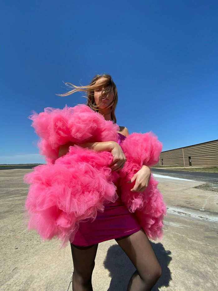 Woman wearing a bold pink fluffy outfit outdoors under blue sky, showcasing confident and entitled patient style demands.