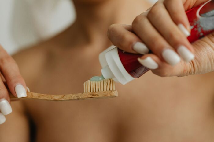 Close-up of a person applying toothpaste on a wooden toothbrush, illustrating messy roommate bathroom habits.