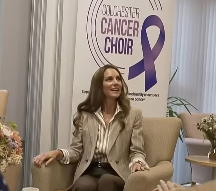 Kate Middleton sitting by Colchester Cancer Choir banner, discussing cancer and its impact on daily function.