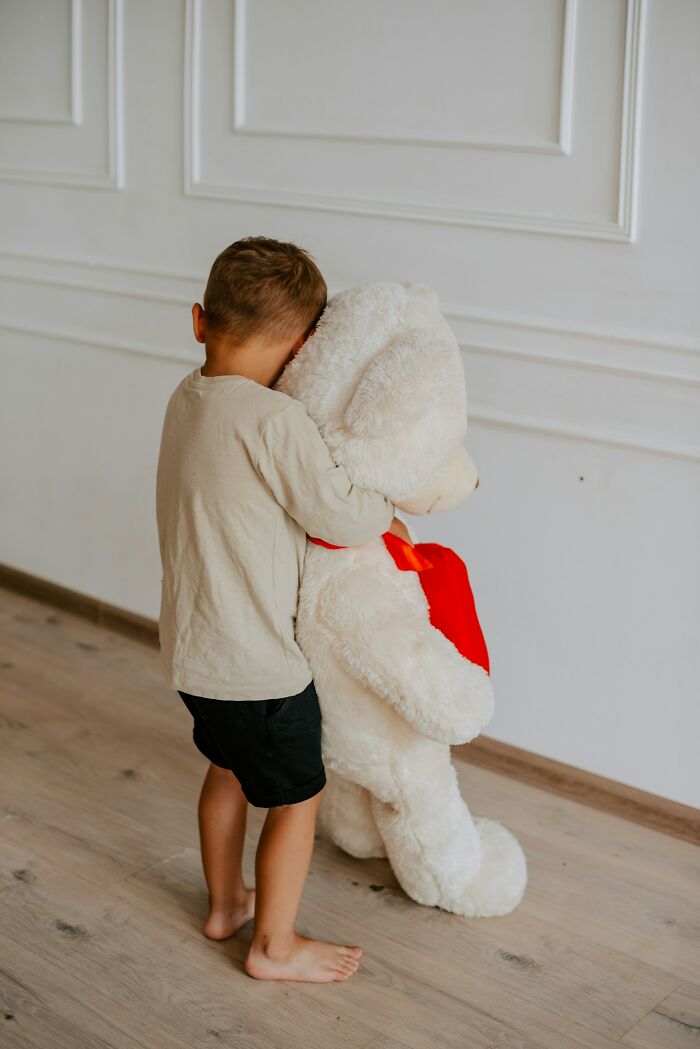 Child hugging a large teddy bear in an empty room, illustrating the impact of parents punishing their kids too far.