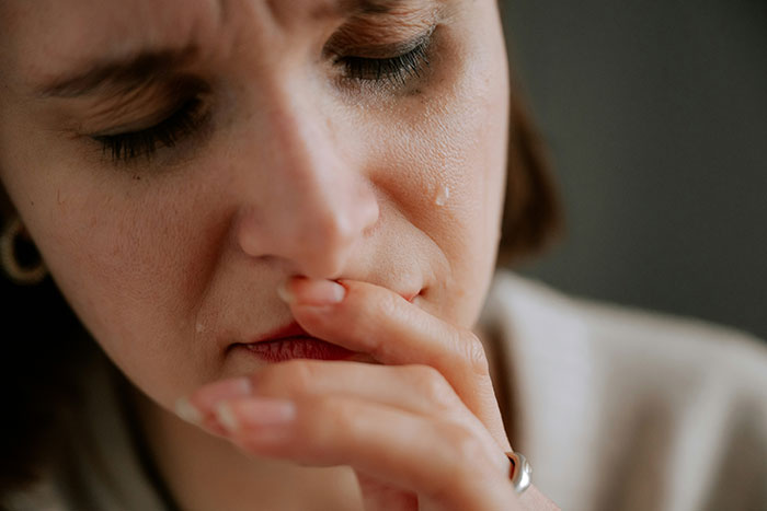 Close-up of a woman crying and touching her lips, expressing sadness and emotional distress over family vacation conflict.