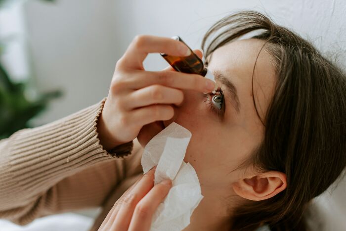 Young woman applying eye drops with tissue in hand, illustrating rare phobias related to eye care and discomfort - 2