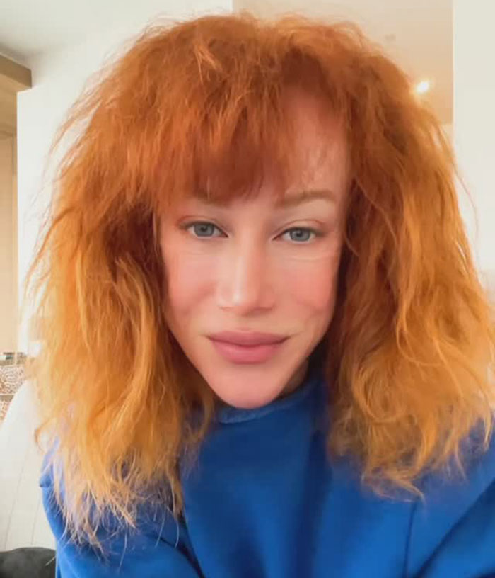 Close-up of a person with natural red hair and blue eyes wearing a blue top, showcasing Kathy Griffin's natural transformation.