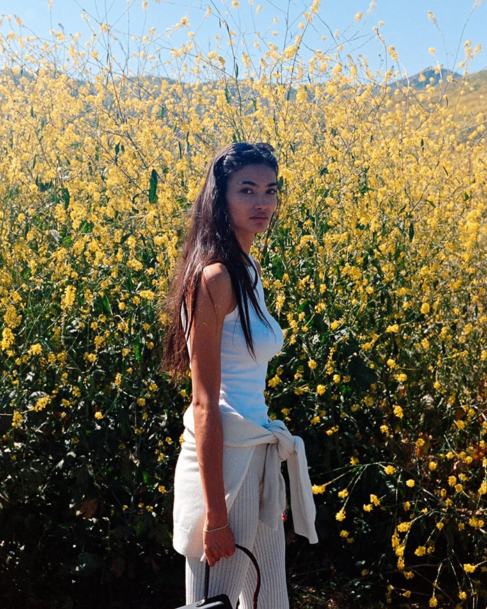 Kelly Gale standing outdoors near yellow flowers wearing a white top and light pants, linked to top model Photoshop blunder.