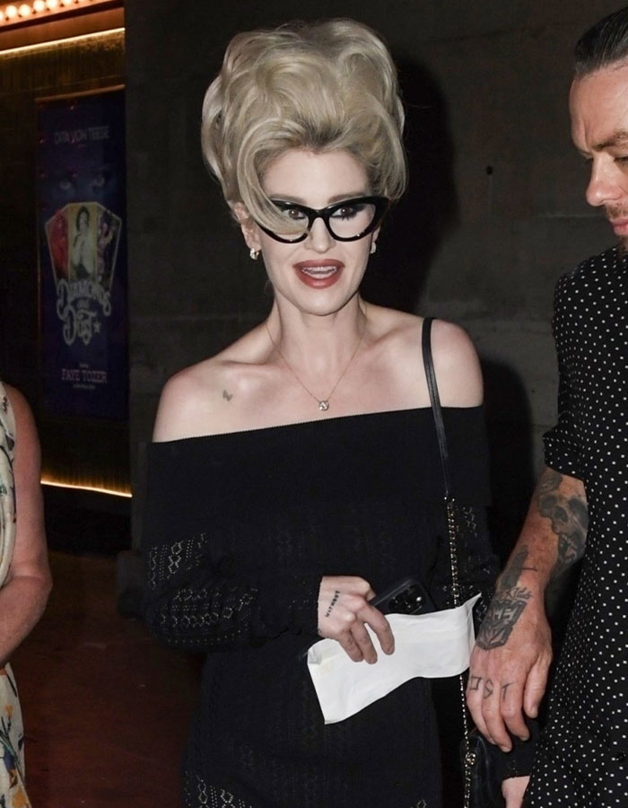 Kelly Osbourne wearing 90s glam fashion with bold hairstyle and black off-shoulder dress at a nighttime event. Kelly Osbourne wearing 90s glam fashion with bold hairstyle and black off-shoulder dress at a nighttime event.