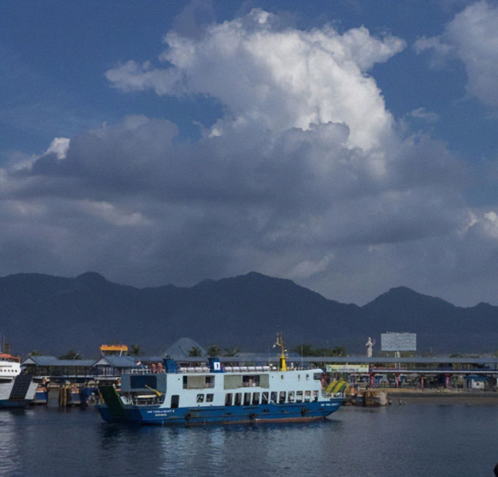 Ferry docked at Bali port with mountains and cloudy sky, related to ferry sank off Bali disaster and missing persons.