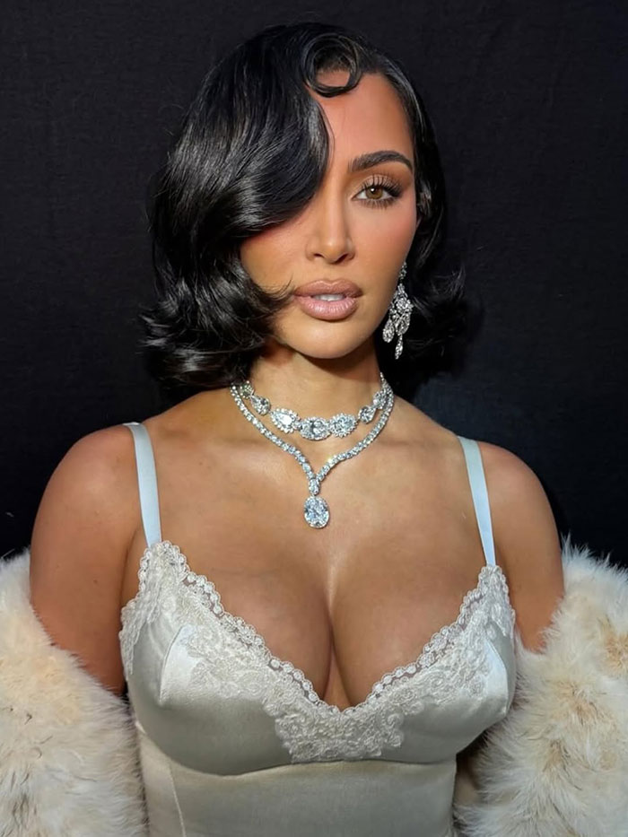 Kim Kardashian wearing elegant jewelry and a satin lace dress, posing with styled hair at a fashion event. Kim Kardashian wearing elegant jewelry and a satin lace dress, posing with styled hair at a fashion event.