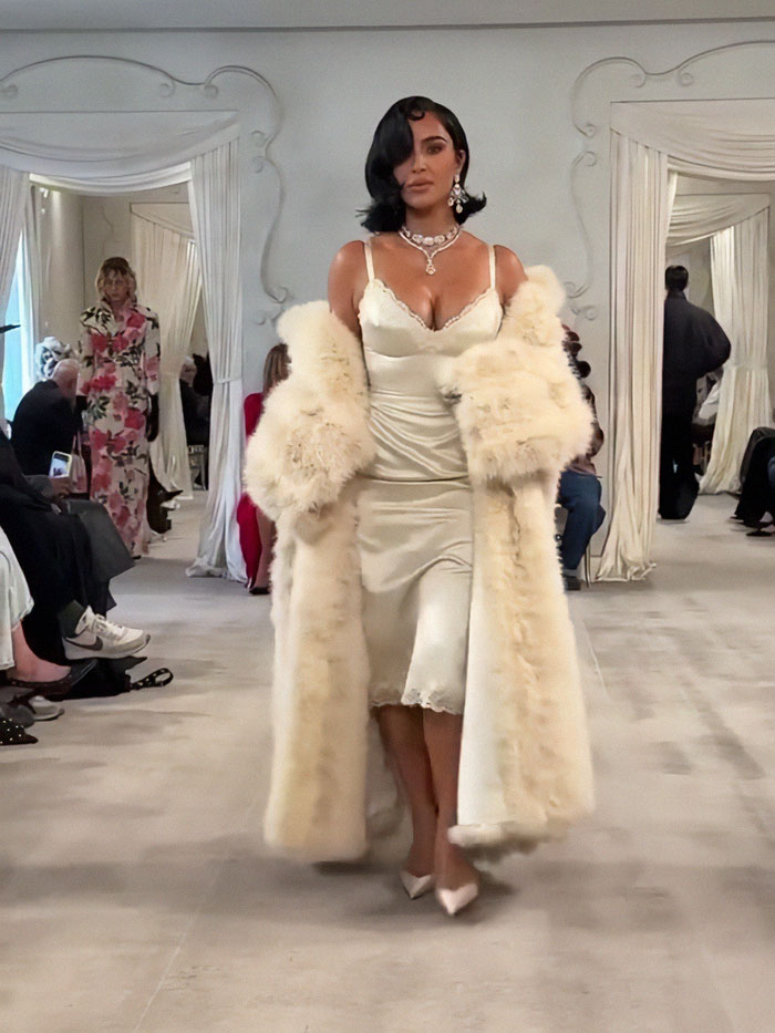 Kim Kardashian walking runway at Paris Fashion Week 2025, wearing a cream satin dress and fur coat in a luxurious setting. Kim Kardashian walking runway at Paris Fashion Week 2025, wearing a cream satin dress and fur coat in a luxurious setting.