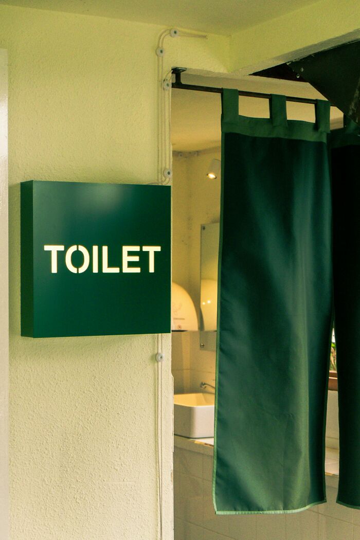 Green toilet sign and curtain at restroom entrance illustrating things men find normal but seem bizarre to women.