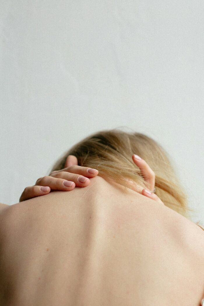 Person touching their bare upper back, illustrating weird things their bodies do that they don’t understand.