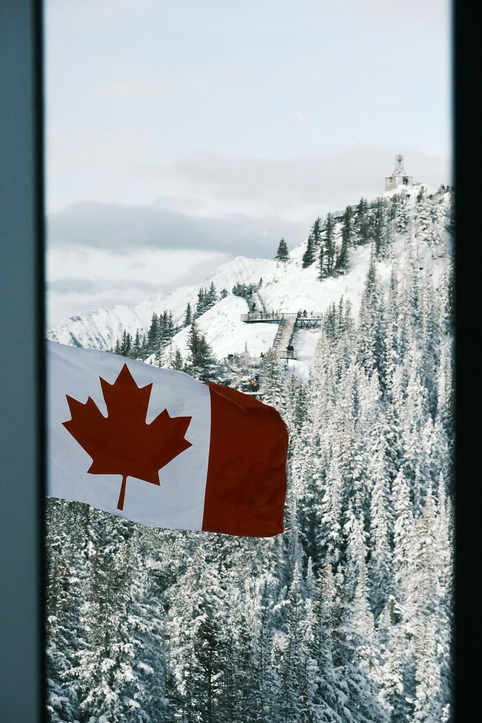 Canadian flag waving outside a window with snowy mountain landscape, symbolizing people who ran away from home. - 22