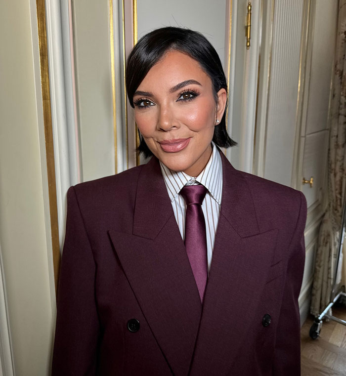 Close-up of Kris Jenner smiling, wearing a maroon suit and tie, related to skeleton Barbie leg Photoshop fail controversy.