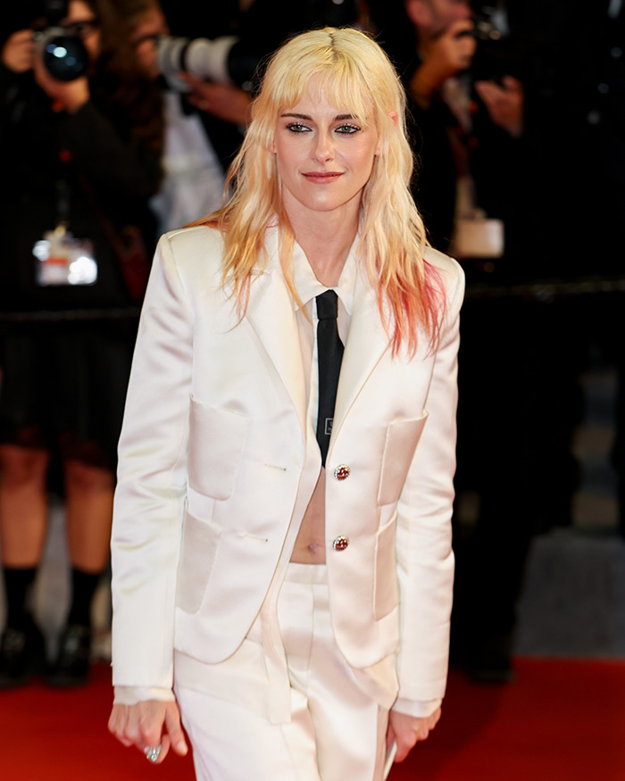 Kristen Stewart in a white suit showcasing a dramatic transformation while attending a red carpet event with photographers behind her. Kristen Stewart in a white suit showcasing a dramatic transformation while attending a red carpet event with photographers behind her.