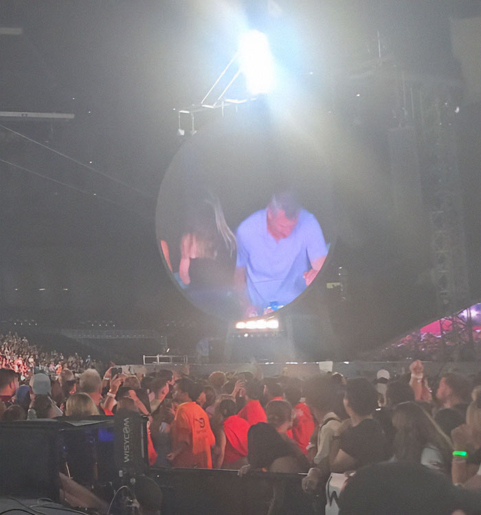 Crowd at Coldplay concert with large round screen showing performer amid bright stage lights and security staff. - 14
