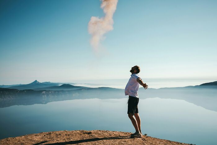 Person standing on a cliff overlooking a lake with arms outstretched, reflecting on things that improved life. - 15