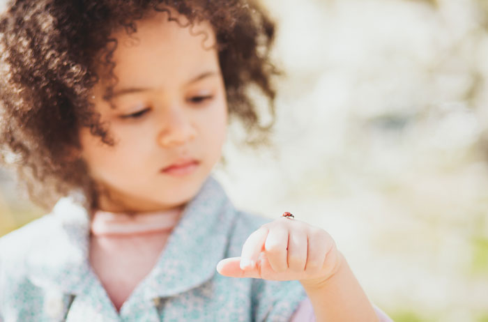Young girl observing a ladybug resting on her finger outdoors, highlighting the ladybug as a symbol of good luck. - 7