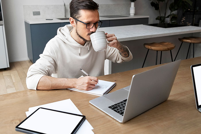 Man working on laptop and taking notes while drinking coffee, illustrating person getting laid off and landing a better job. Man working on laptop and taking notes while drinking coffee, illustrating person getting laid off and landing a better job.
