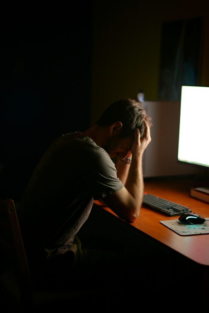 Man sitting at a computer desk, holding his head in frustration, illustrating men share things that seem bizarre to women.