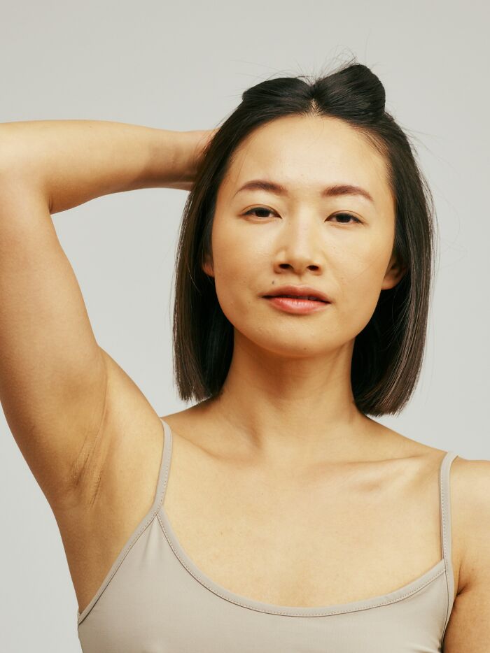 Young woman with mysterious body quirk posing confidently in a beige tank top against a neutral background.