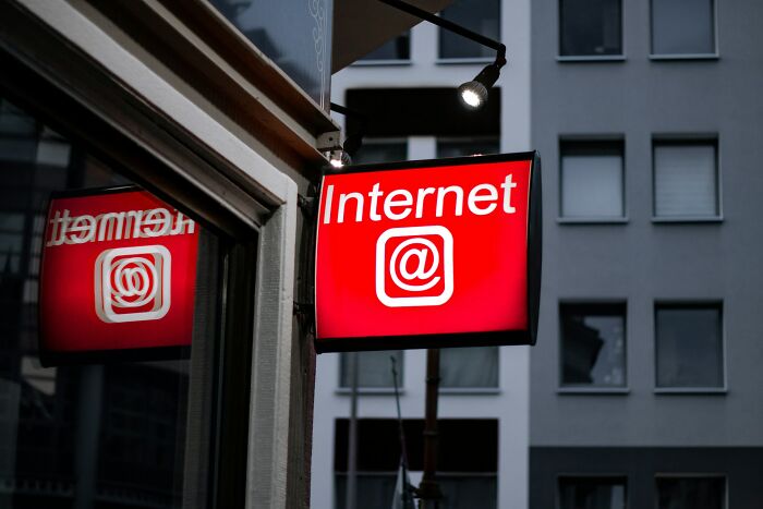 Red illuminated sign with the word Internet and at symbol outside a building in an urban setting. - 17