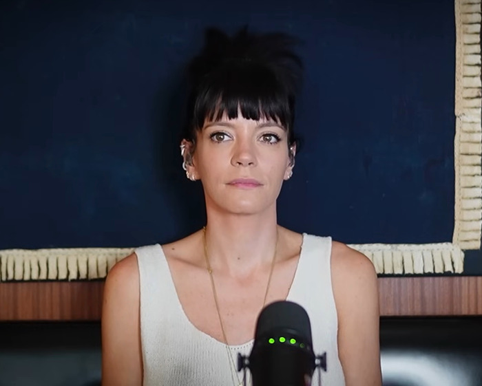 Lily Allen speaking into a microphone with a neutral expression, highlighting her abortion confession controversy.