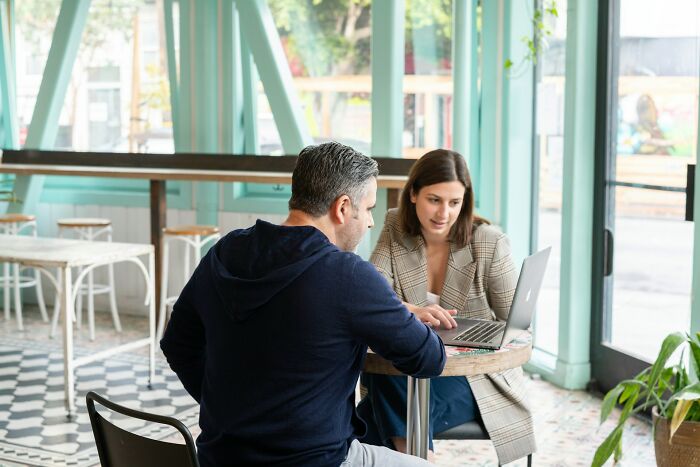 Two professionals discussing six figure jobs while looking at a laptop in a modern cafe with natural light.