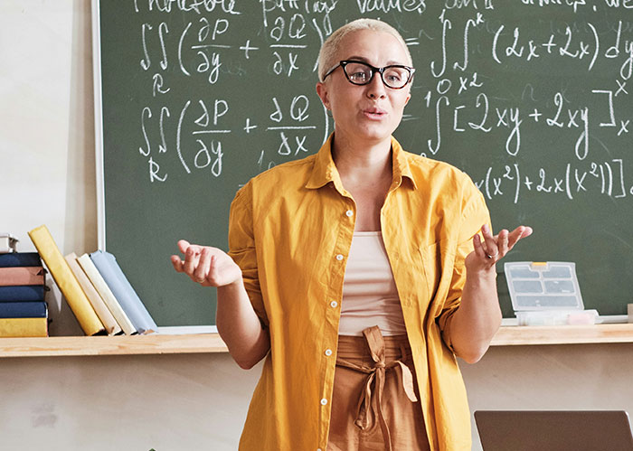 Teacher standing in front of a chalkboard with math formulas, illustrating concerns about the literacy crisis in US education.